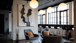 Un área de descanso moderna con sillones contemporáneos, un cuadro abstracto de gran tamaño y ventanas amplias que dejan entrar luz natural.