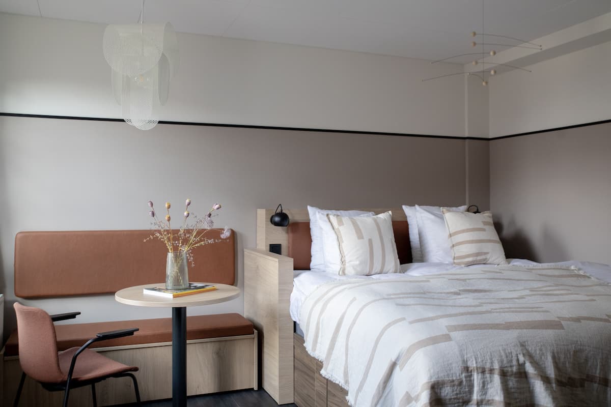 Een moderne slaapkamer met een bed, nachtkastje en een zithoek met een stoel en een kleintje tafel.