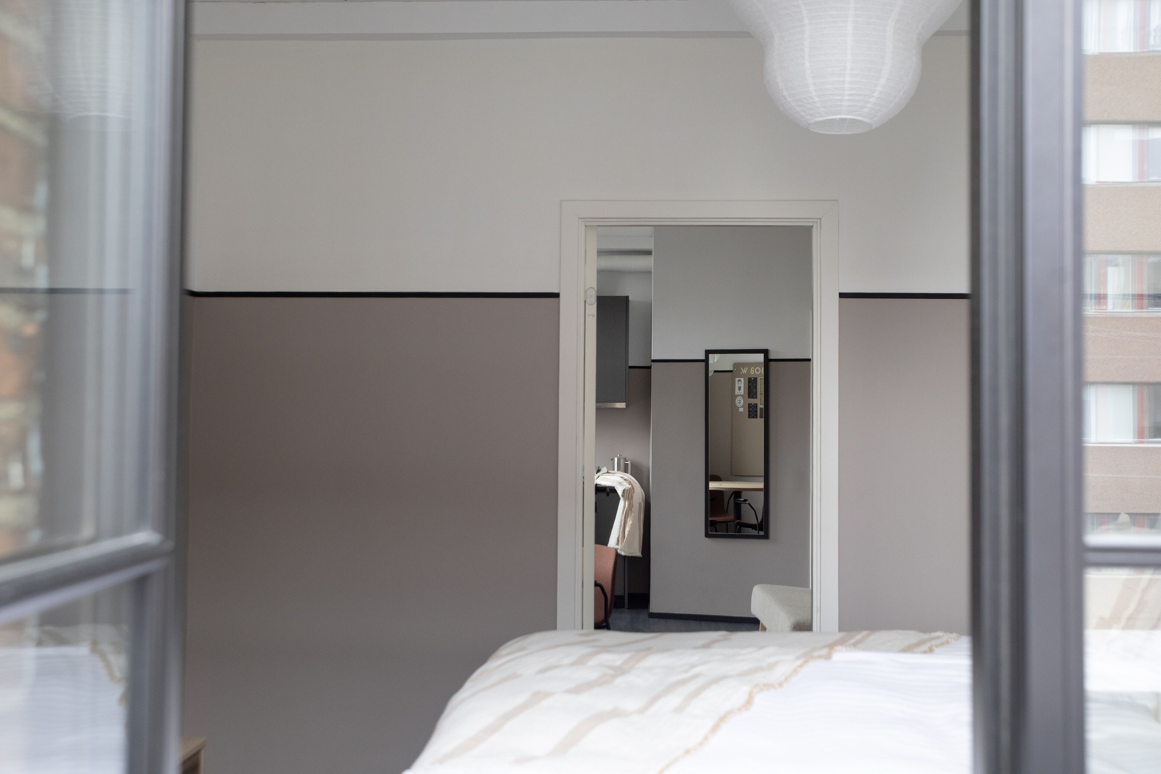 Habitación de hotel con cama, espejo y vista a un pasillo con perchero.