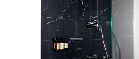 Un baño con baldosas de mármol negro, cabina de ducha de vidrio y tres botellas de champú y acondicionador en un estante.
