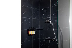 Une salle de bain avec des carreaux de marbre noir, une douche en verre et trois bouteilles de shampoing et d’après-shampoing posées sur une étagère.