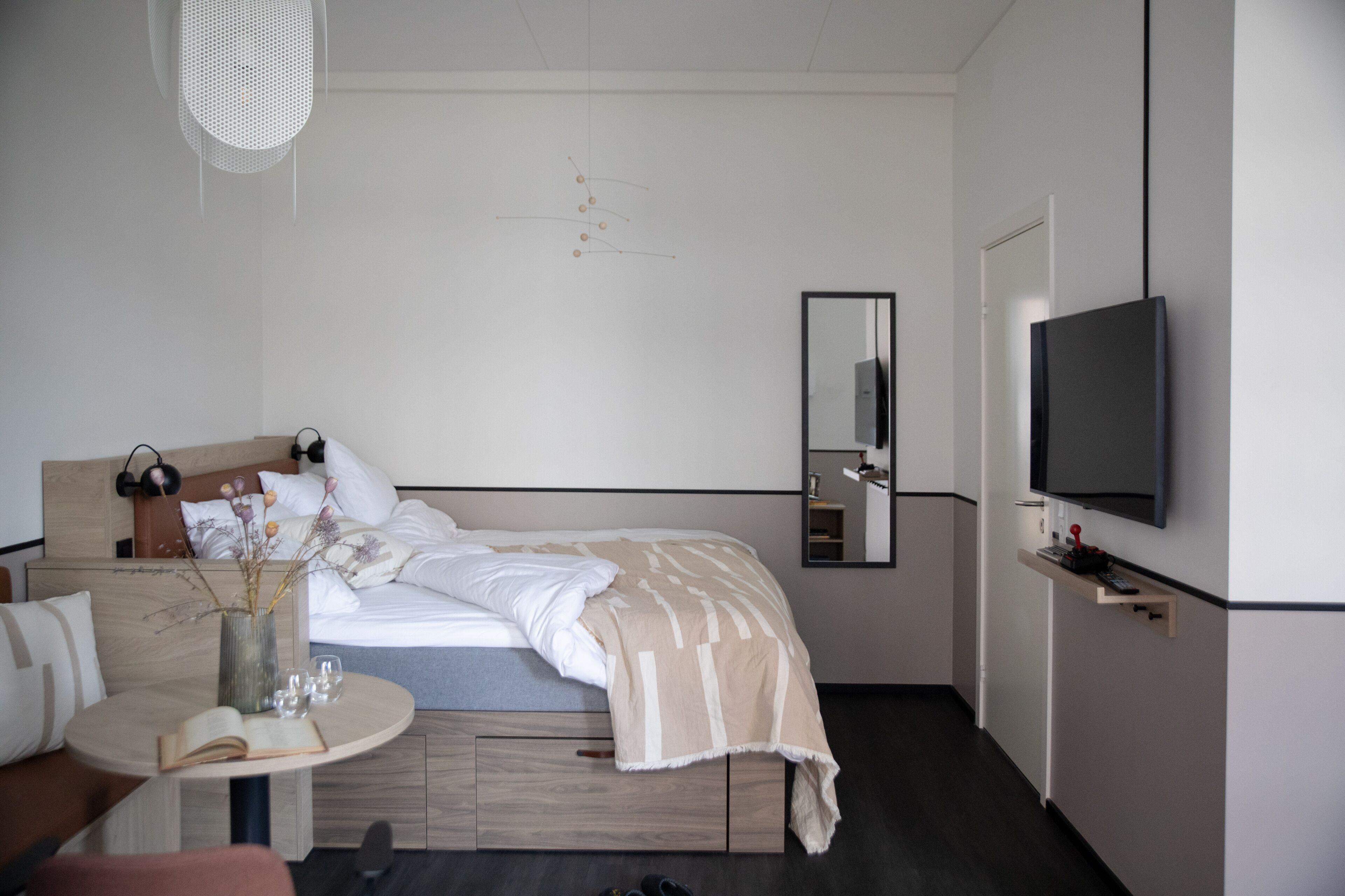 A modern hotel room with a bed, bedside table, TV, and a mirror.