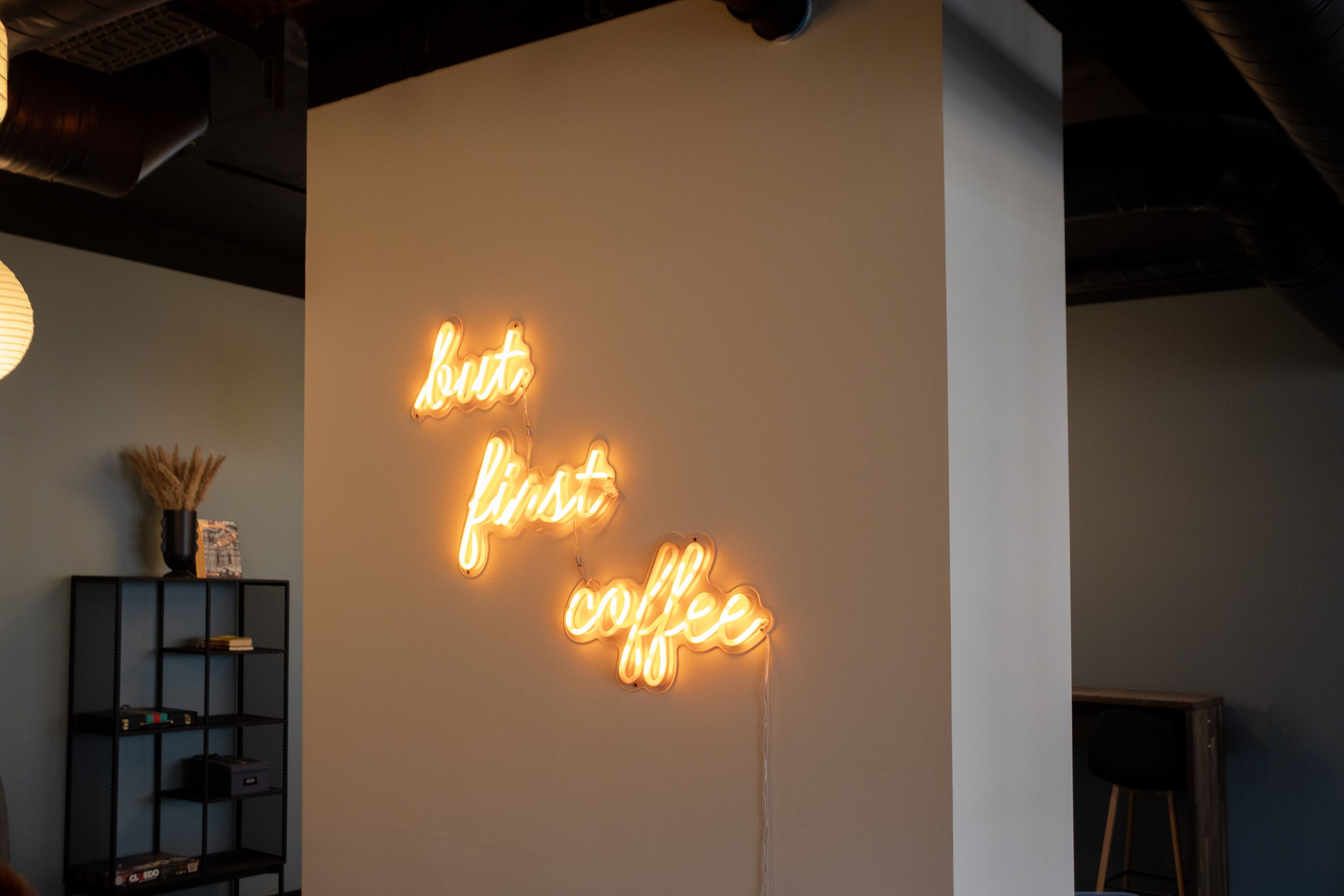 A neon sign on a wall that reads "but first coffee".