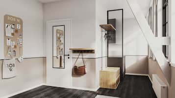 A modern interior with a white door, a bulletin board, a coat rack, a small wooden chest, and a staircase.
