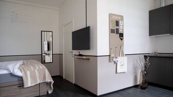 A modern hotel room with a bed, a TV, a small kitchenette, and a mirror.