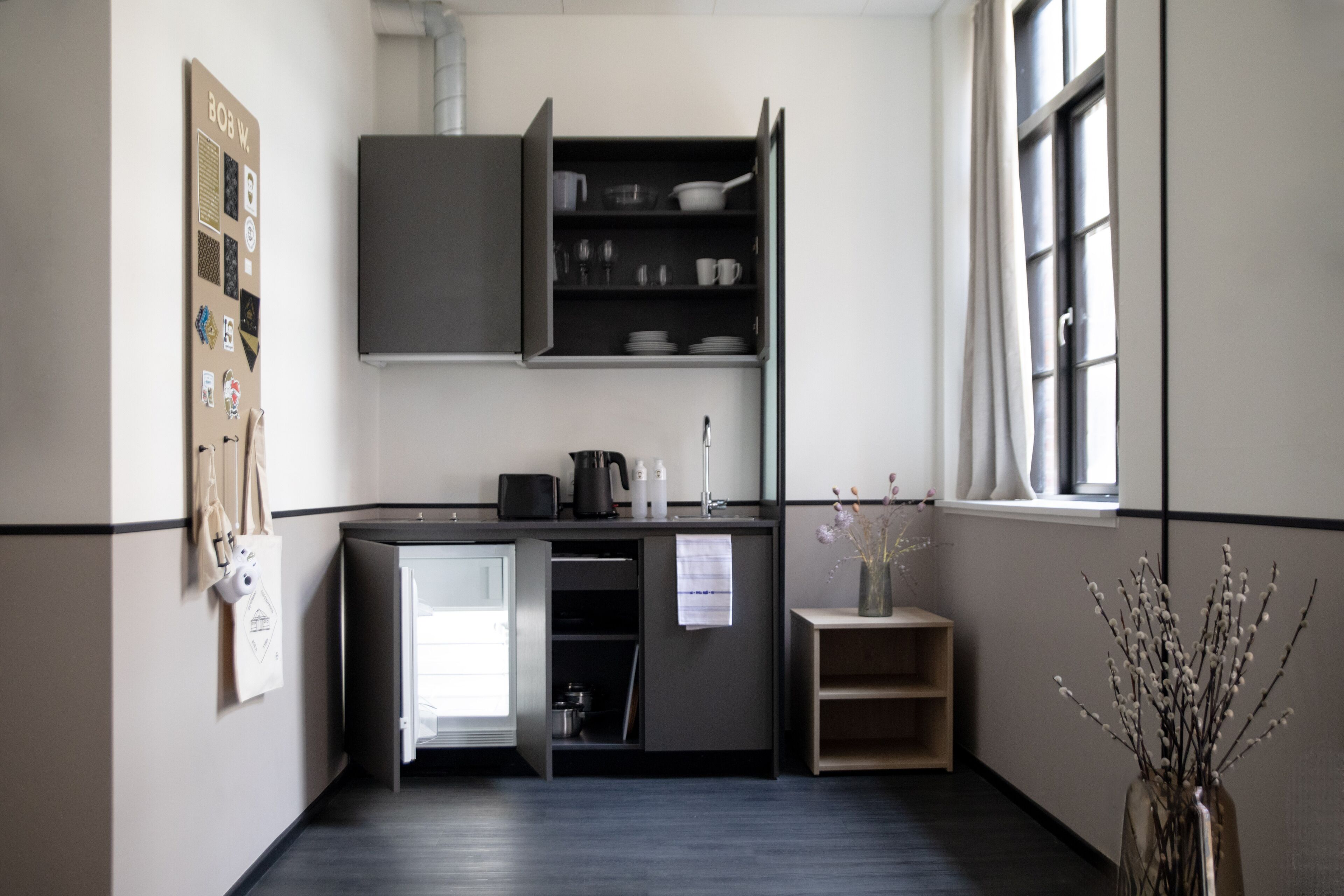 A compact kitchen with a refrigerator, a coffee maker, and a small shelf.