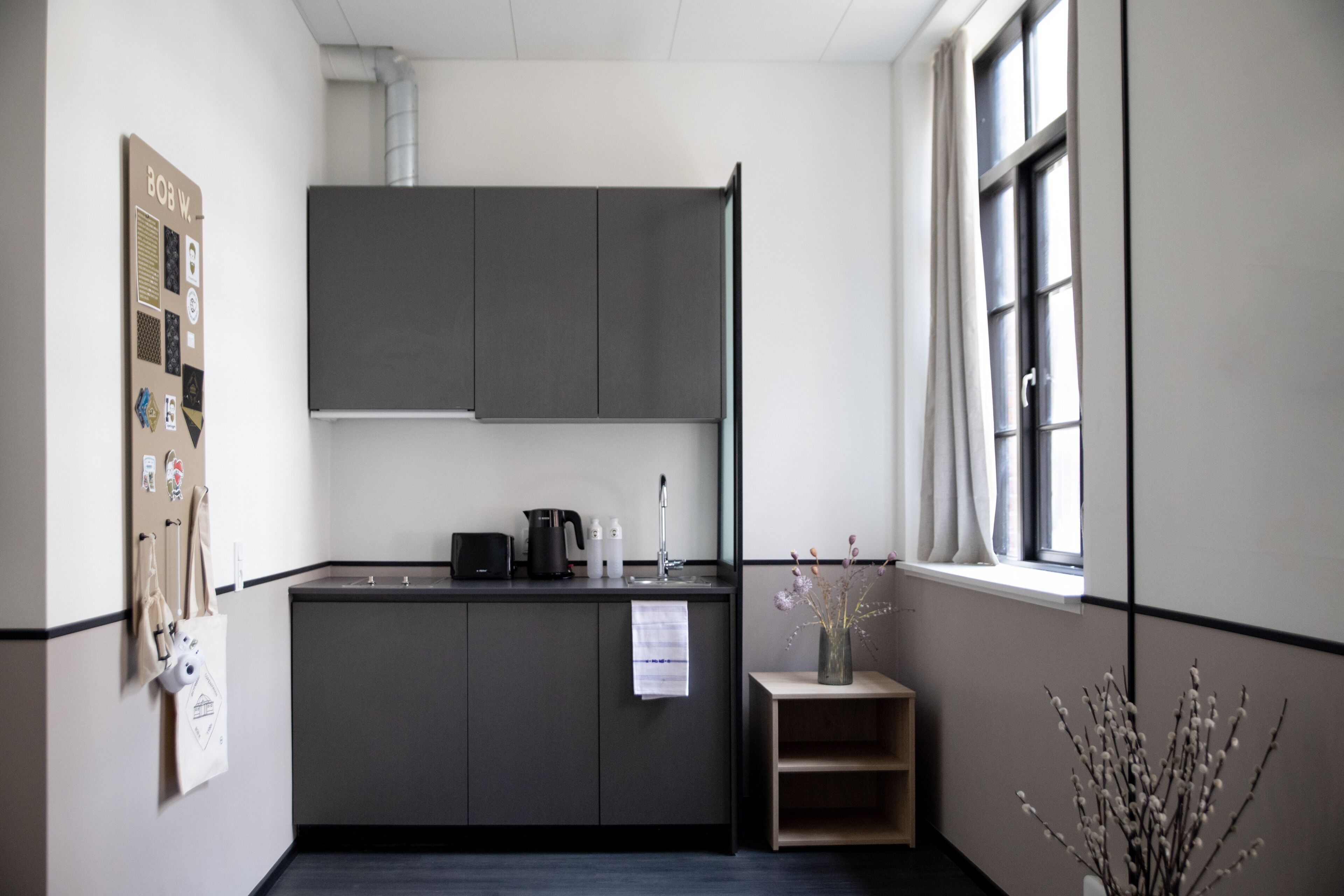 A modern kitchen with grey cabinets, a coffee machine, and a small window with a view.