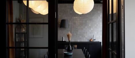 A modern dining area with a dark wooden table, black chairs, and a vase of dried flowers. A large, round, white paper lantern hangs from the ceiling.