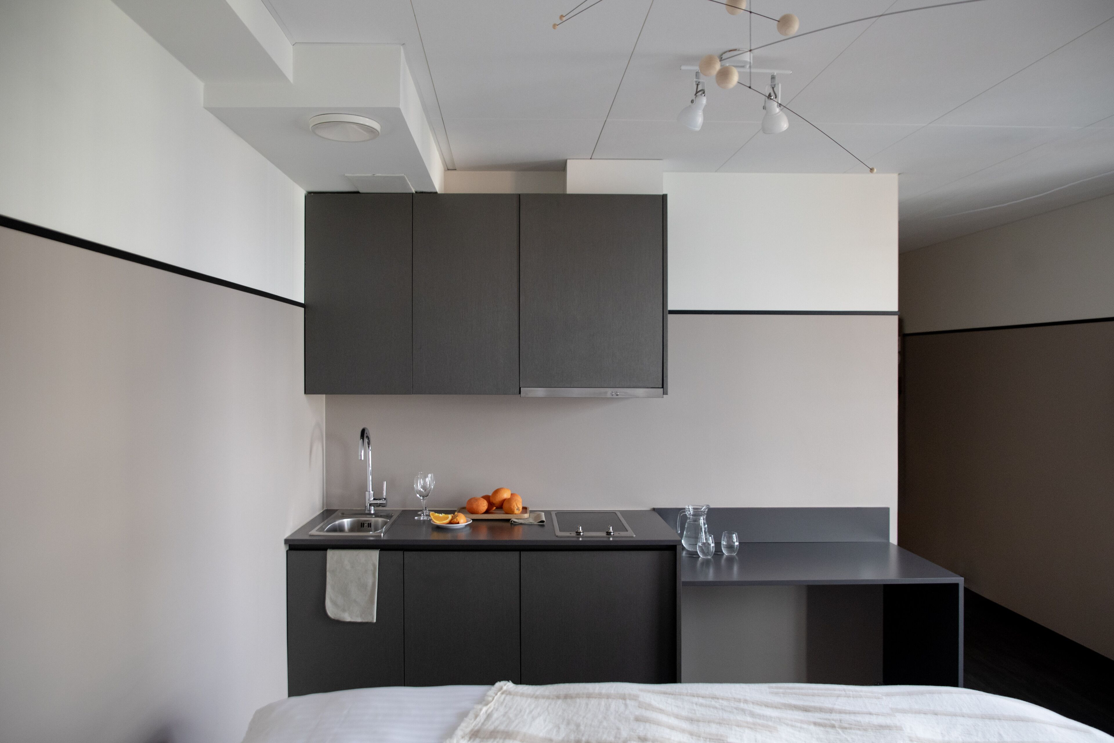 Una habitación de hotel moderna y funcional con kitchenette, cama y un pequeño comedor.