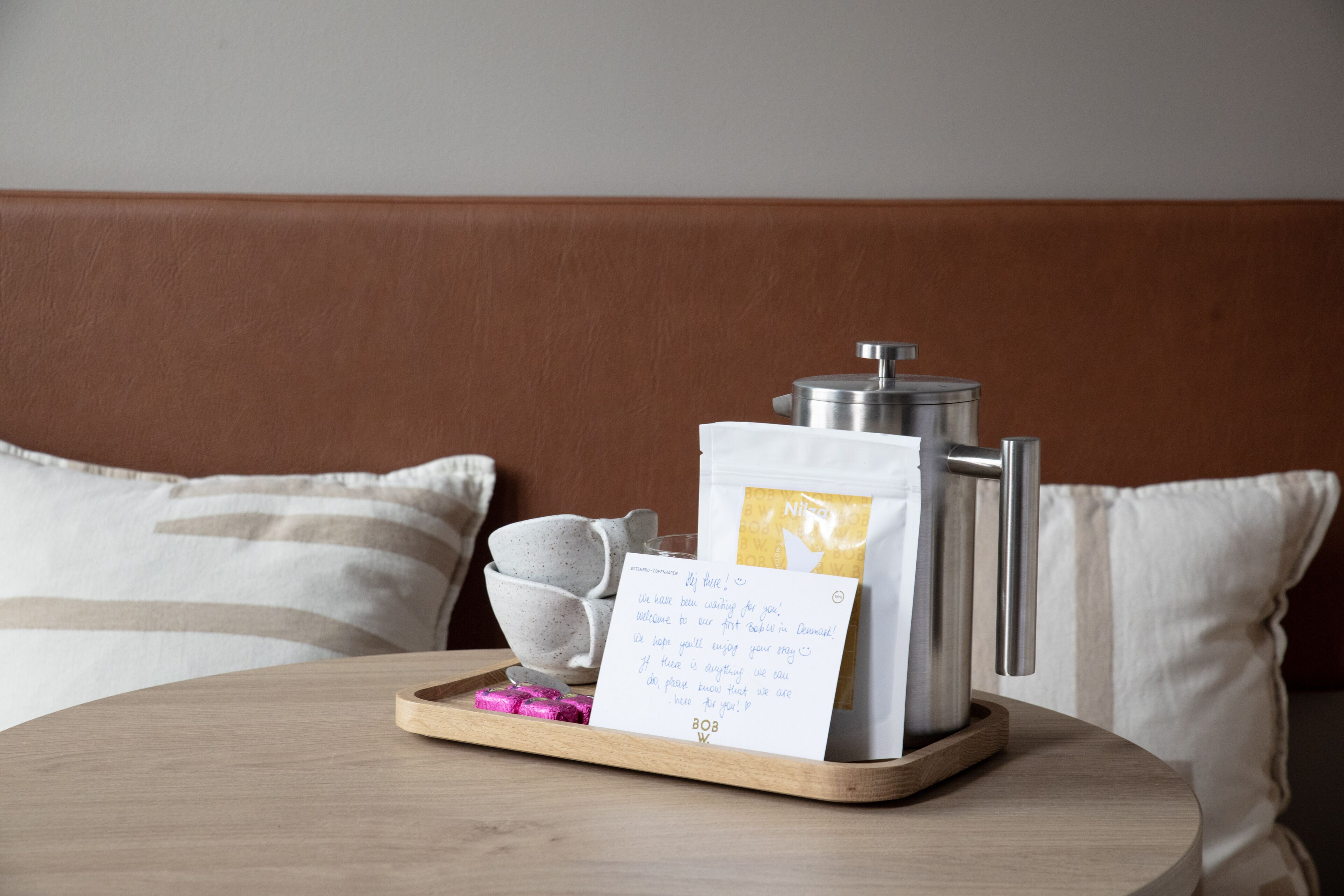 A wooden tray with a coffee pot, a card, and a cup on a table in a hotel room.