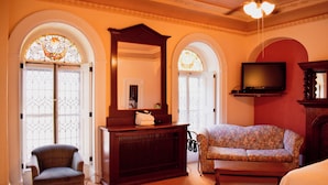 A room with a large wooden cabinet, a television mounted on the wall, a floral sofa, and a chair. - Hotel Terrasse Dufferin (Québec City)