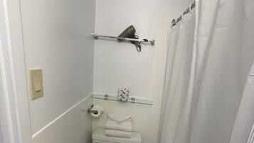 A small, compact bathroom with a toilet, a glass shelf above the toilet, and a shower curtain.
