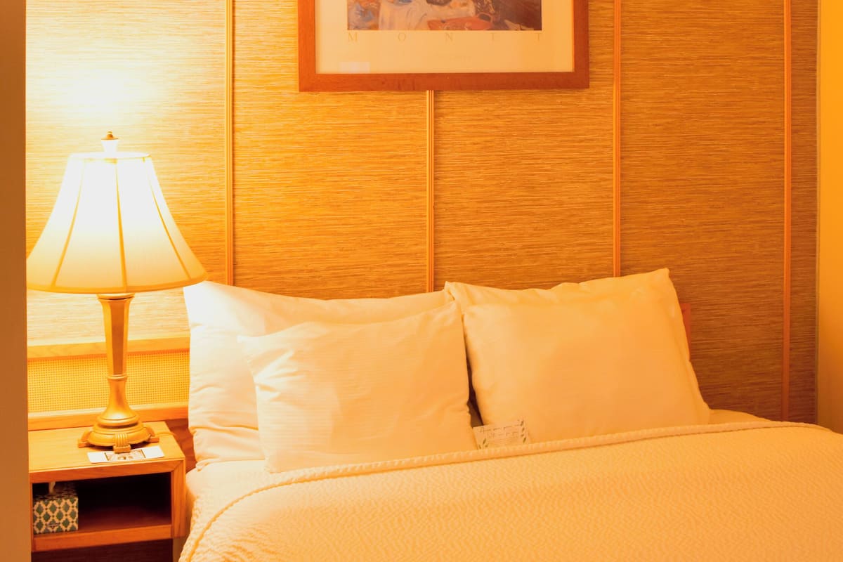 A hotel room with a bed, a nightstand, a lamp, and a framed picture on the wall.