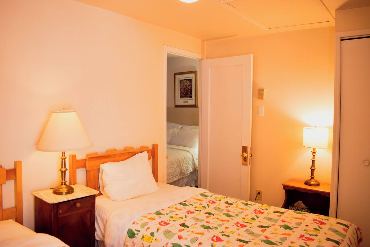 A hotel room with a bed, two bedside tables with lamps, a door, and a wall-mounted light fixture.