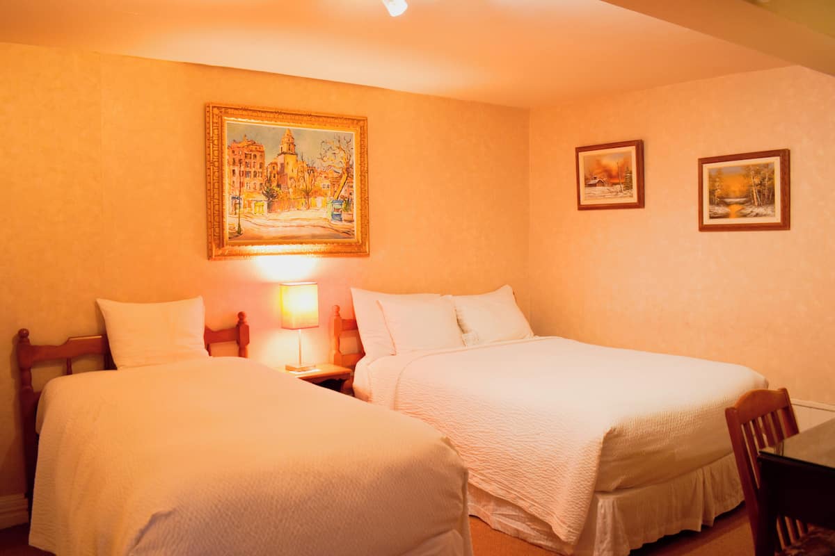 A hotel room with two single beds, a nightstand with a lamp, and two framed pictures on the wall.