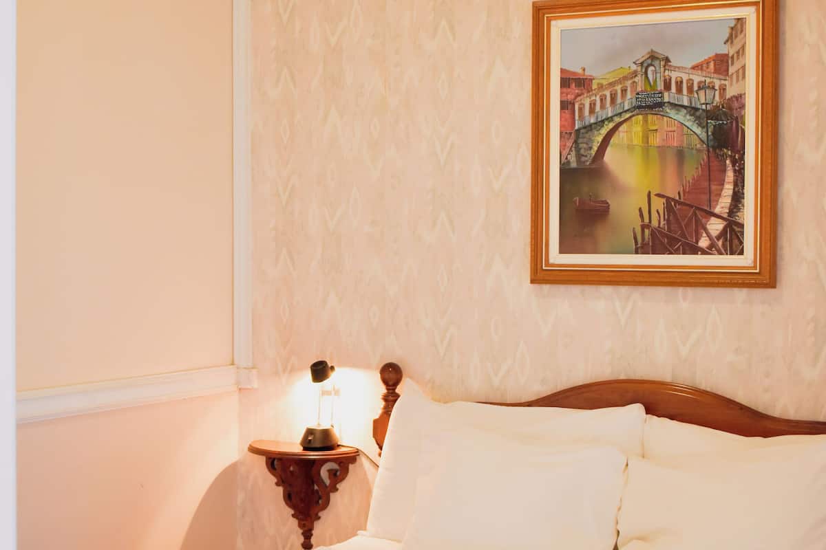 A neatly made bed with white linens, a wooden headboard, and a nightstand with a lamp.