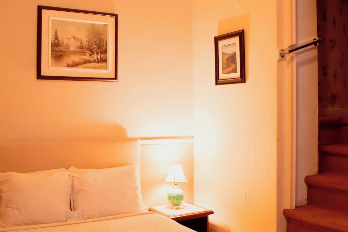 A hotel room with a bed, a nightstand with a lamp, and a framed picture on the wall.