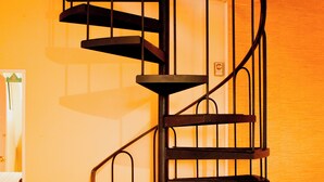 A spiral staircase in a room with a wooden floor and a table with a floral tablecloth. - Hotel Terrasse Dufferin (Québec City)