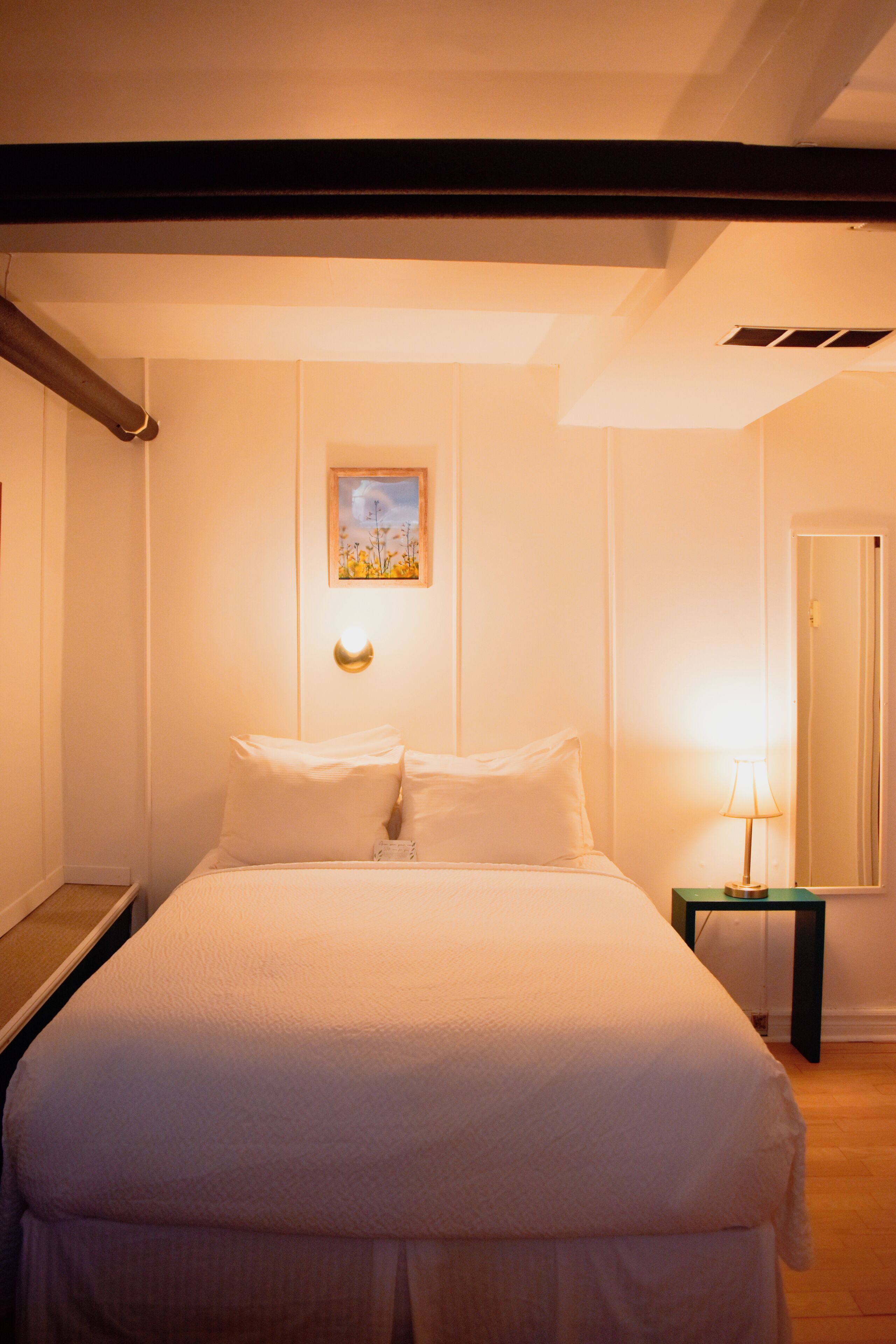A neatly made bed with white linens in a room with a wooden floor and white walls.