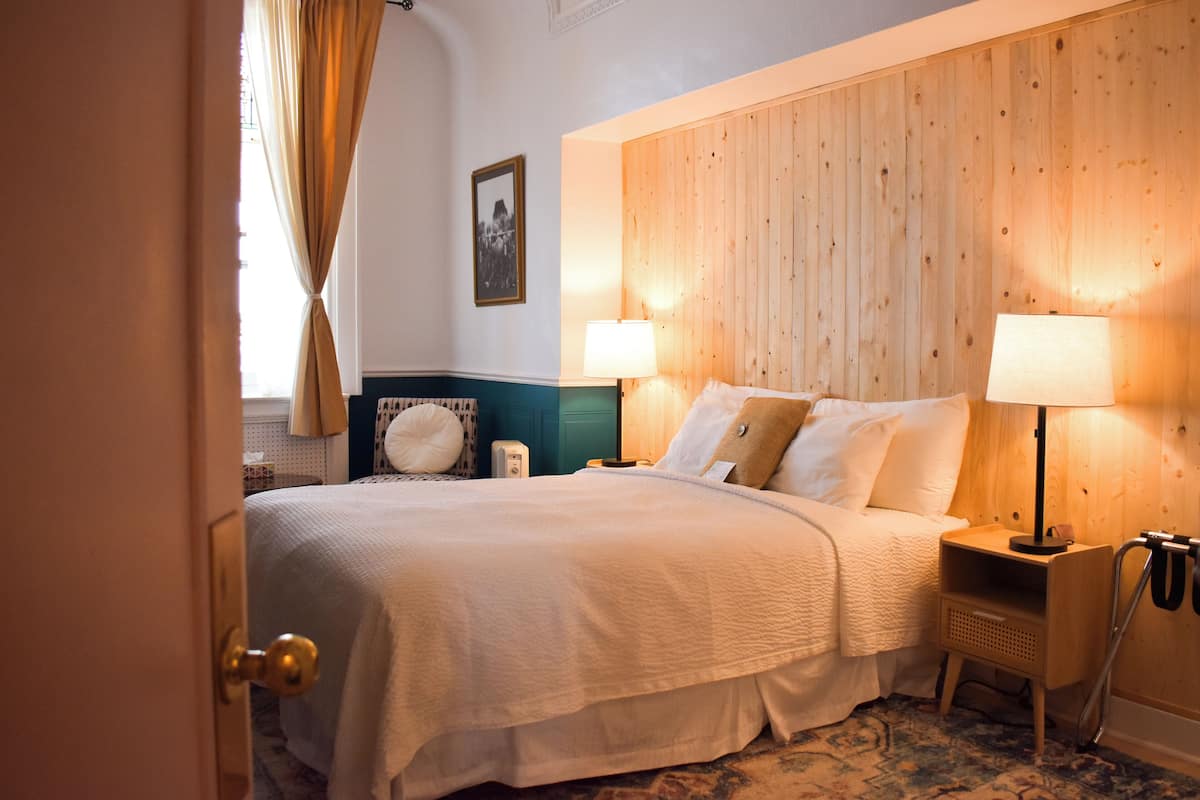 A hotel room with a large bed, two bedside tables with lamps, a wooden headboard, a wall-mounted picture, and a patterned carpet.