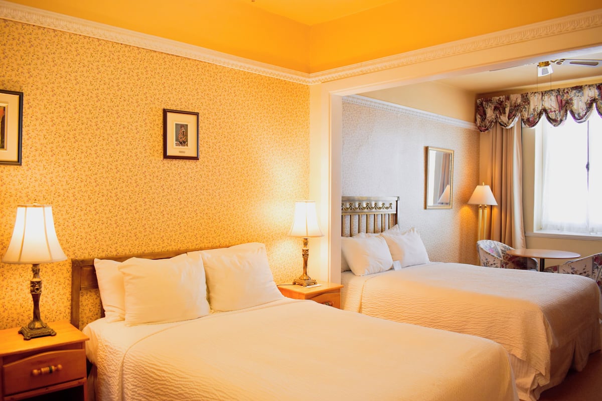 A hotel room with two beds, a small table, and two lamps.