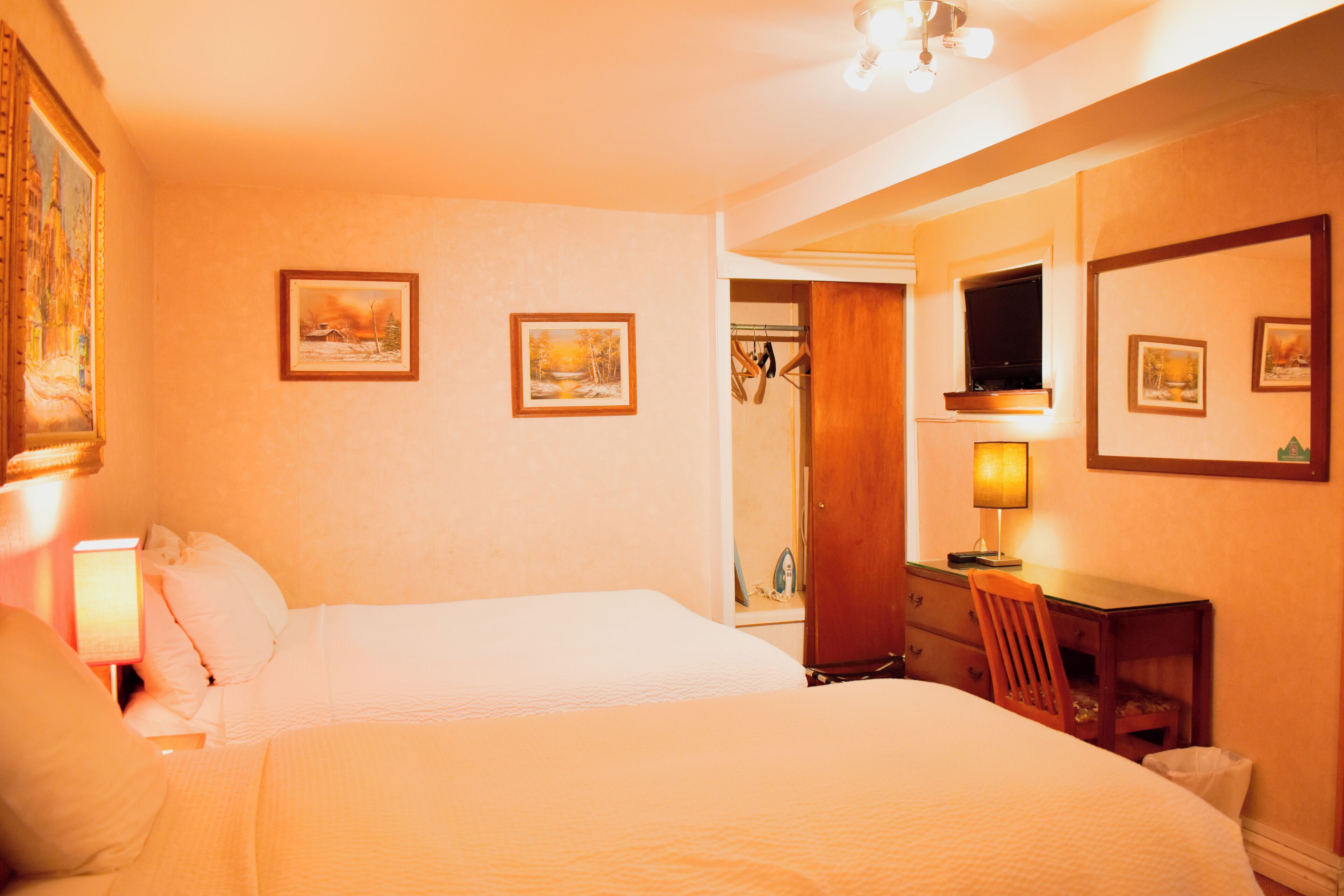 A hotel room with two beds, a desk with a chair, a TV, and framed pictures on the walls.