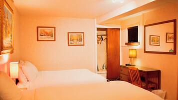 A hotel room with two beds, a desk with a chair, a TV, and framed pictures on the walls.