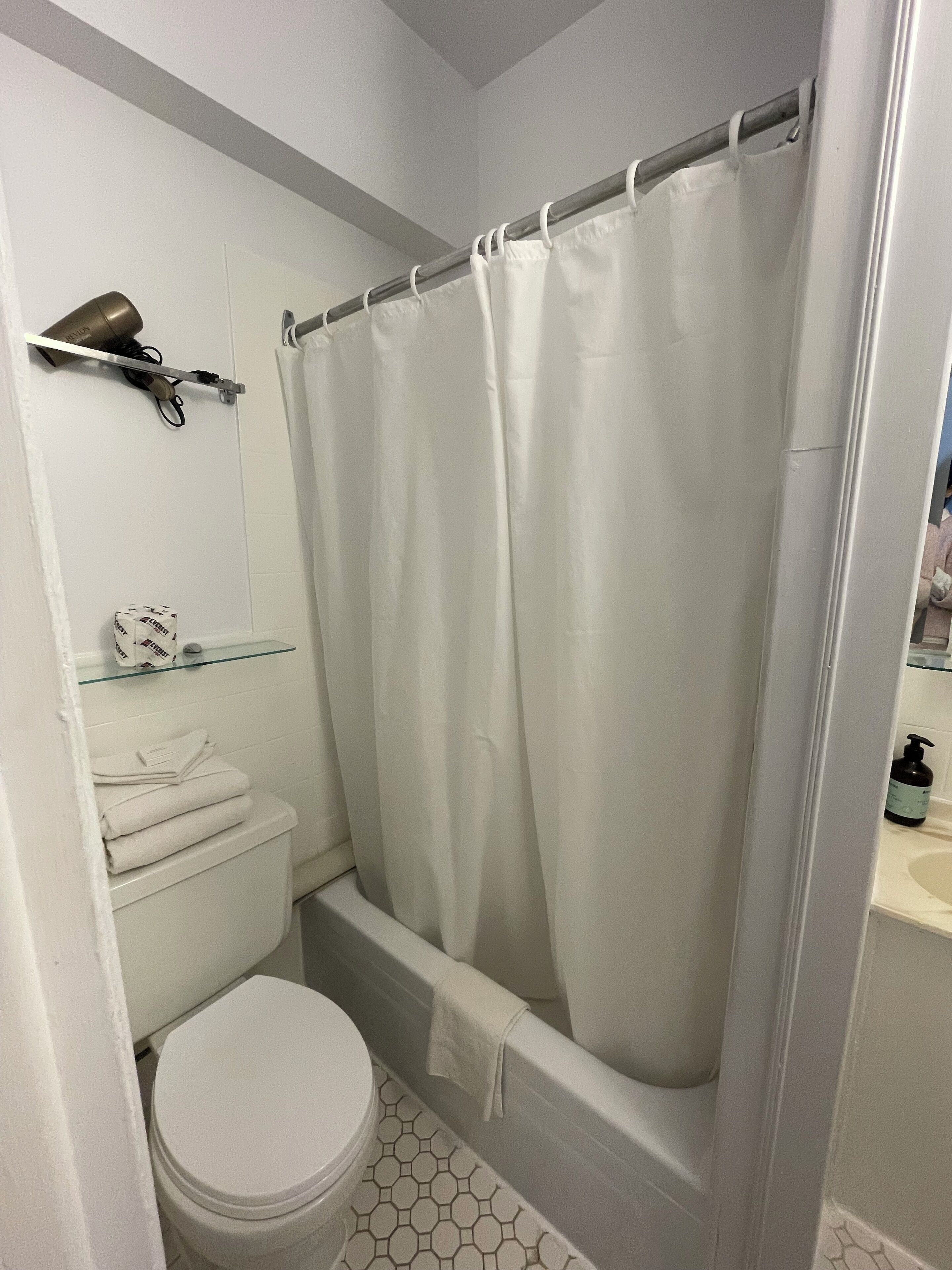 Une salle de bain équipée de toilettes, d’un rideau de douche et d’une étagère contenant des articles de toilette.