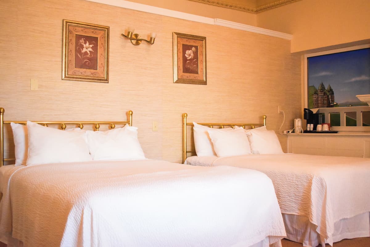 A hotel room with two beds, a painting of a castle, and a wall-mounted lamp.