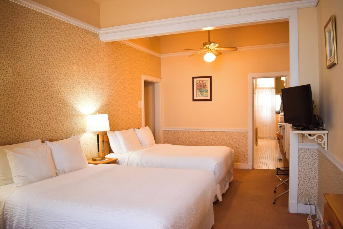 A hotel room with two beds, a desk with a computer, a ceiling fan, and a framed picture on the wall.