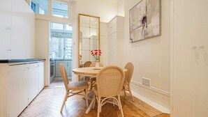 A dining area with a round table, wicker chairs, and a vase with red flowers. - Beautiful Belgravia by Underthedoormat (London)