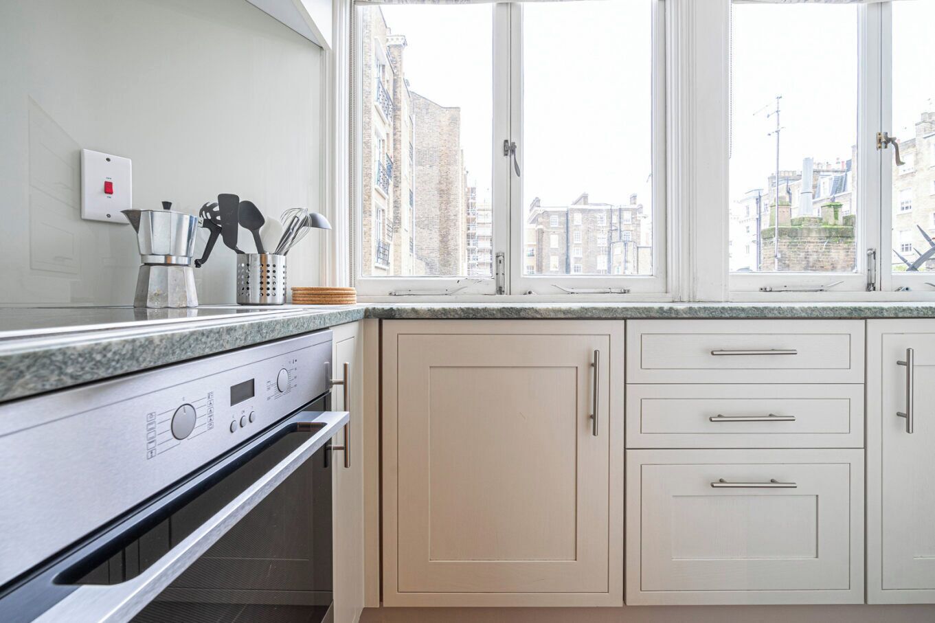 A modern kitchen with a built-in oven, a coffee machine, and a window with a city view.