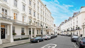 A row of white, classic buildings with uniform architecture, parked cars, and a clear blue sky. - Beautiful Belgravia by Underthedoormat (London)