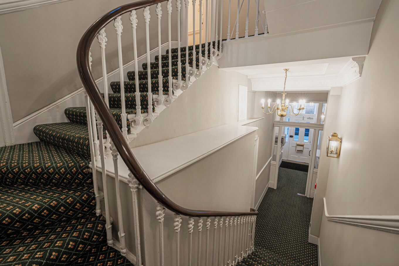 A grand staircase with ornate white railings and patterned carpeted steps.