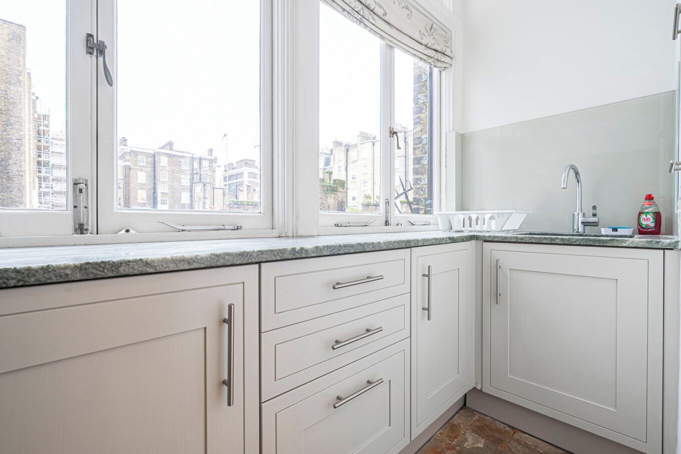 A modern kitchen with white cabinetry, a granite countertop, and a large window offering a city view.