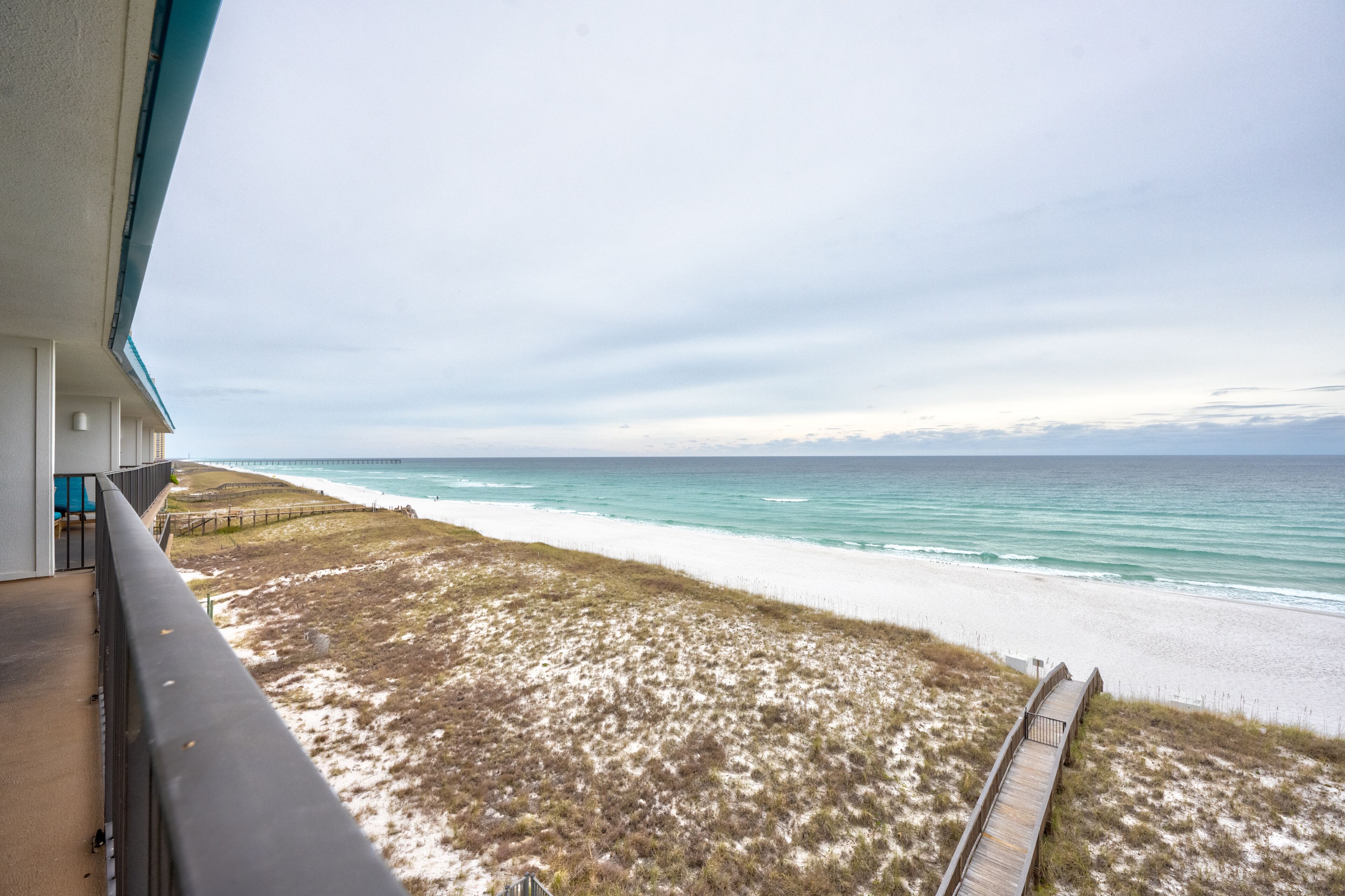 Vista de la playa desde un balcón con un paseo de madera que lleva a la orilla.