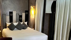 A modern hotel room with a large bed, a seating area, and a unique ceiling light fixture. - Riad Pourpre Medina (Marrakech)