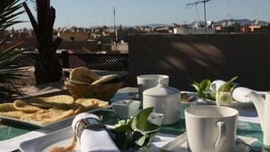 A table set for breakfast on a rooftop with a city view, including plates of food, cups, and a pitcher. - Riad Pourpre Medina (Marrakech)