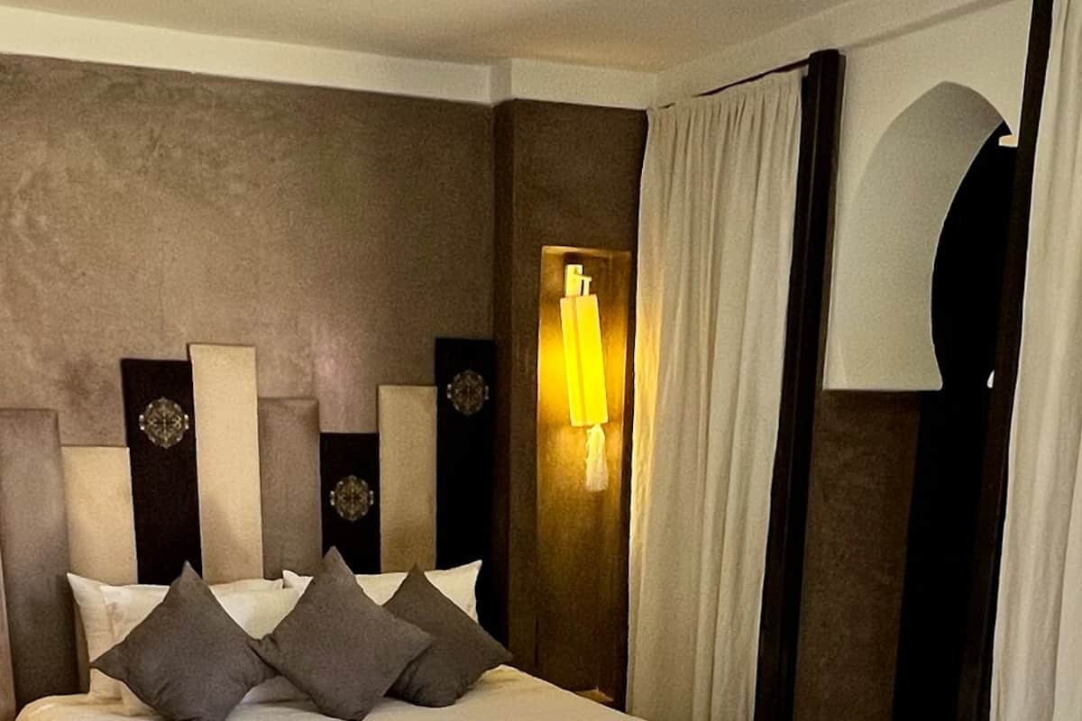 A hotel room with a large bed, a nightstand, a lamp, and a seating area with a table and chairs.