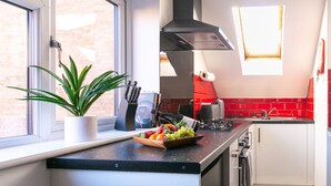 Une cuisine moderne avec une fenêtre, une hotte noire et un panier de fruits posé sur le plan de travail.