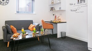 Un salon moderne avec un canapé gris, un fauteuil orange et une petite table à manger où sont disposés des aliments pour le petit-déjeuner.
