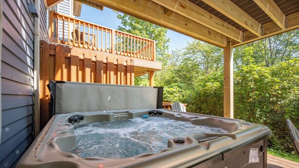 A hot tub on a wooden deck with a wooden railing and a view of trees.