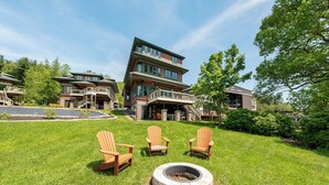 Un bâtiment moderne à deux étages, doté d’une façade en pierre, d’un foyer extérieur et de trois chaises Adirondack, le tout situé dans un espace pelouse bien entretenu.