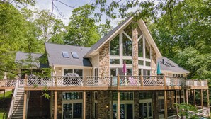 A multi-level house with a stone facade, large windows, and a balcony with a wooden railing.