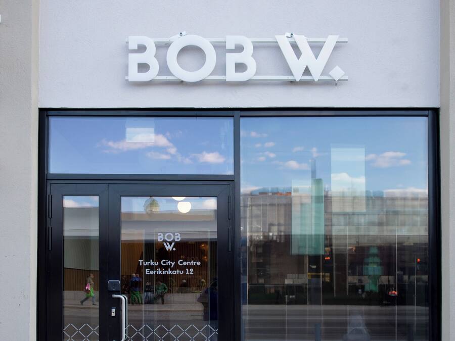 A building with a large glass entrance, a sign reading "BOB W.", and a reflection of a cityscape.