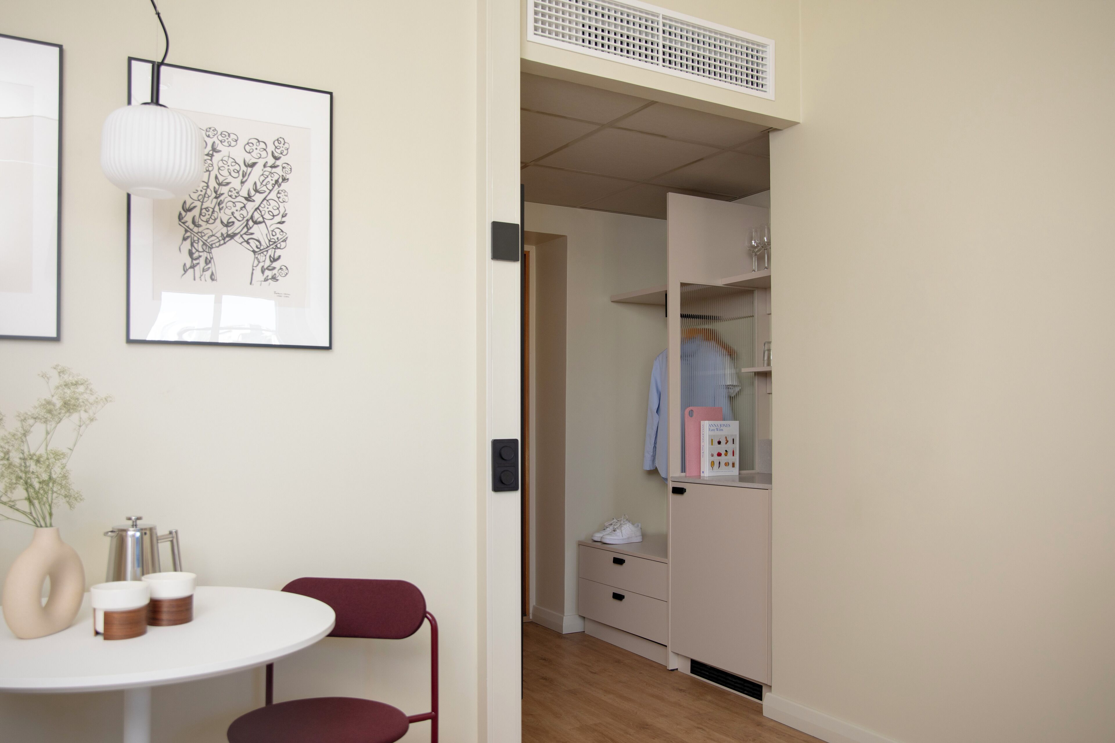 A room with a round table, a chair, a vase with flowers, and a framed picture on the wall.