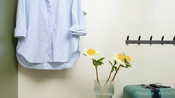 A room with a hanging shirt, a vase with flowers, a suitcase, and a filing cabinet.