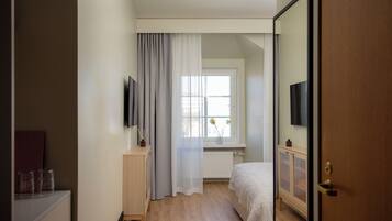 A bedroom with a bed, a window with curtains, a bedside table, and a TV mounted on the wall.