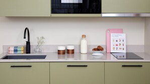 A modern kitchen with a stainless steel sink, a black faucet, a microwave, and a range hood above the stove. There are two jars on the counter, a bottle of milk, and a cookbook titled "Anna Jones Easy Wins". - Bob W Turku City Centre (Turku)