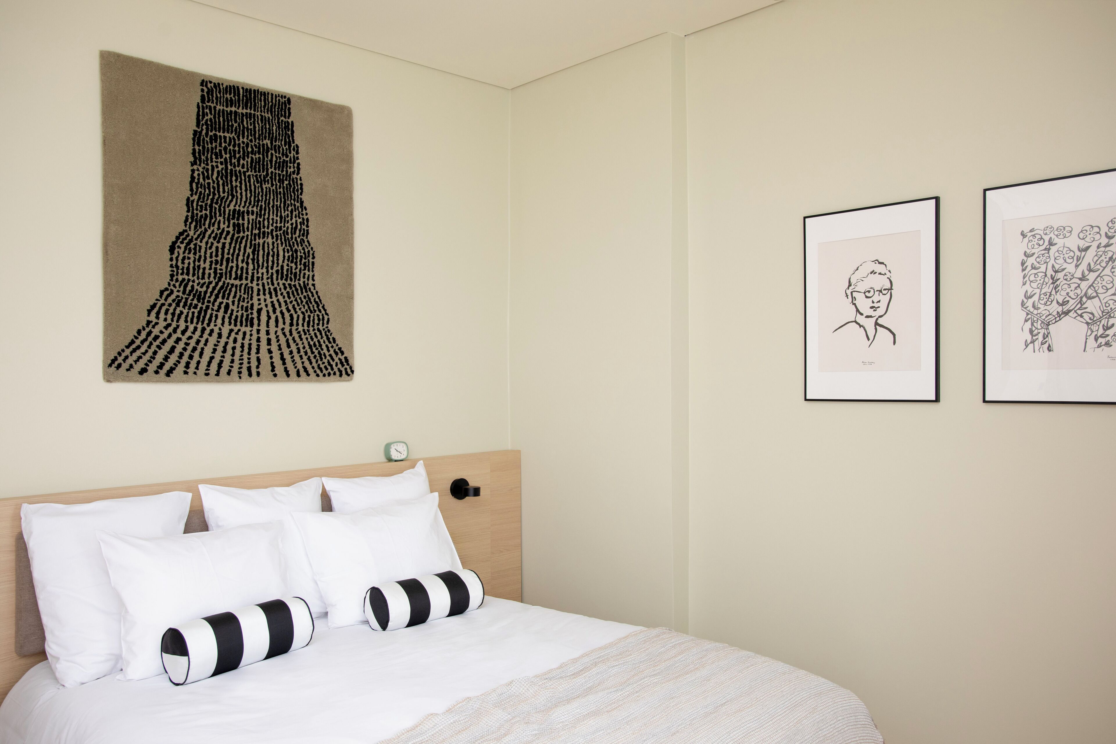 Una habitación de hotel con cama, ropa de cama blanca, cabecero de madera y obras de arte en las paredes.